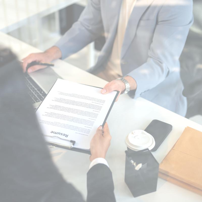 person wearing suit handing a resume to another person also wearing a suit