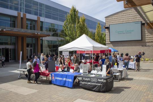 Students and employers interacting at an outdoor campus job fair with tables, tents, and informational booths